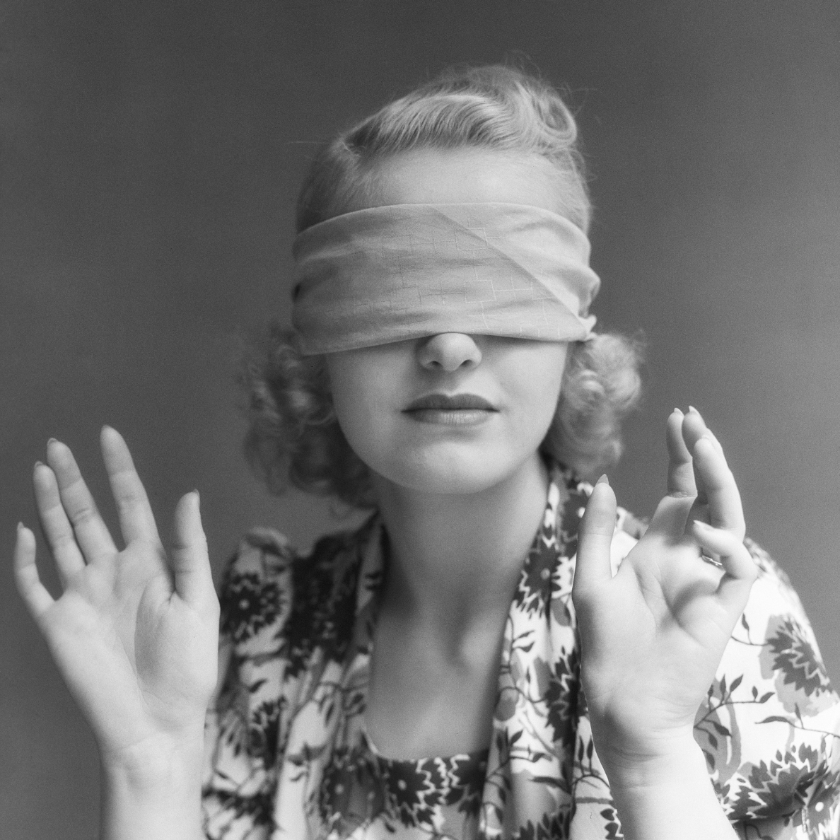Vintage black-and-white photo of a woman blindfolded with a calm expression and raised hands, symbolizing confusion and the need for guidance.