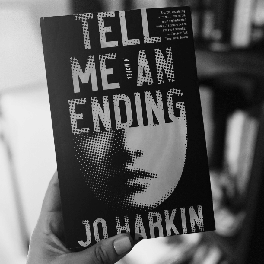 Book titled 'Tell Me An Ending' by Jo Harkin held in a hand with a blurred background