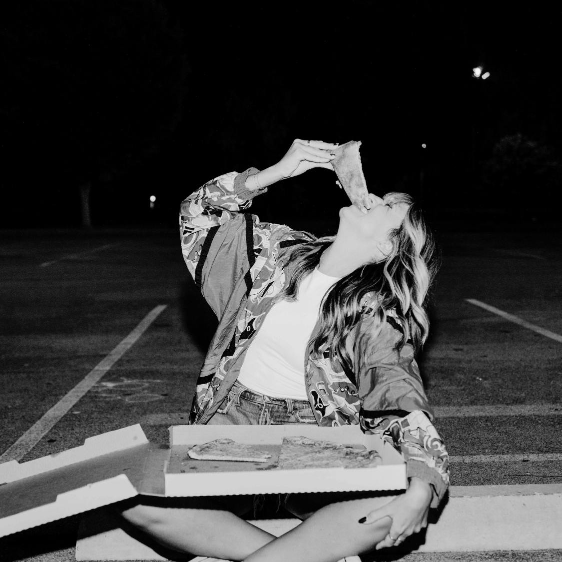 Person sitting on a bench in a parking lot at night, holding a book above their head.
