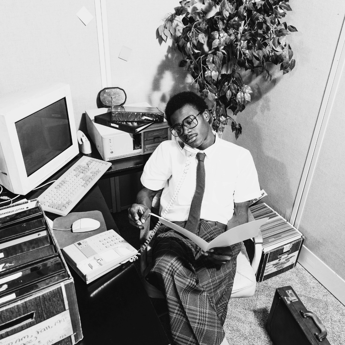 Person sitting in an office cubicle with computer equipment and books.