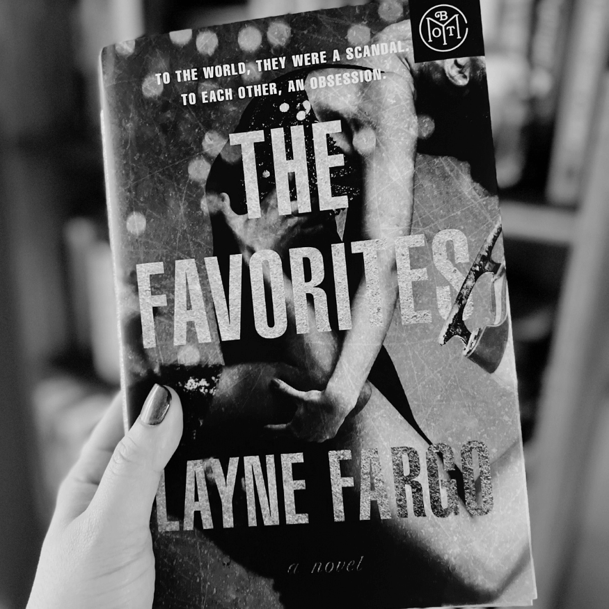 Book titled 'The Favorites' by Layne Fargo held in front of a blurred background