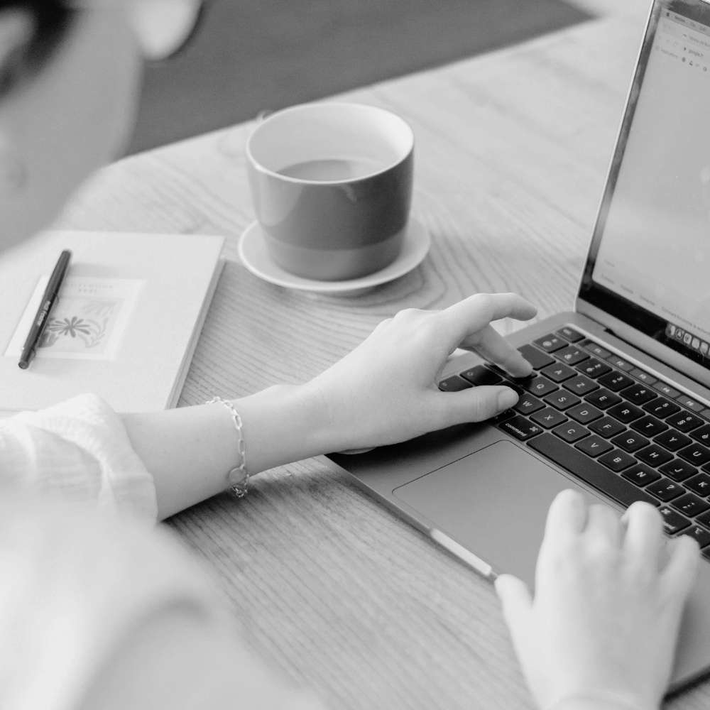 Person using a laptop with a cup of tea and notebook on a desk