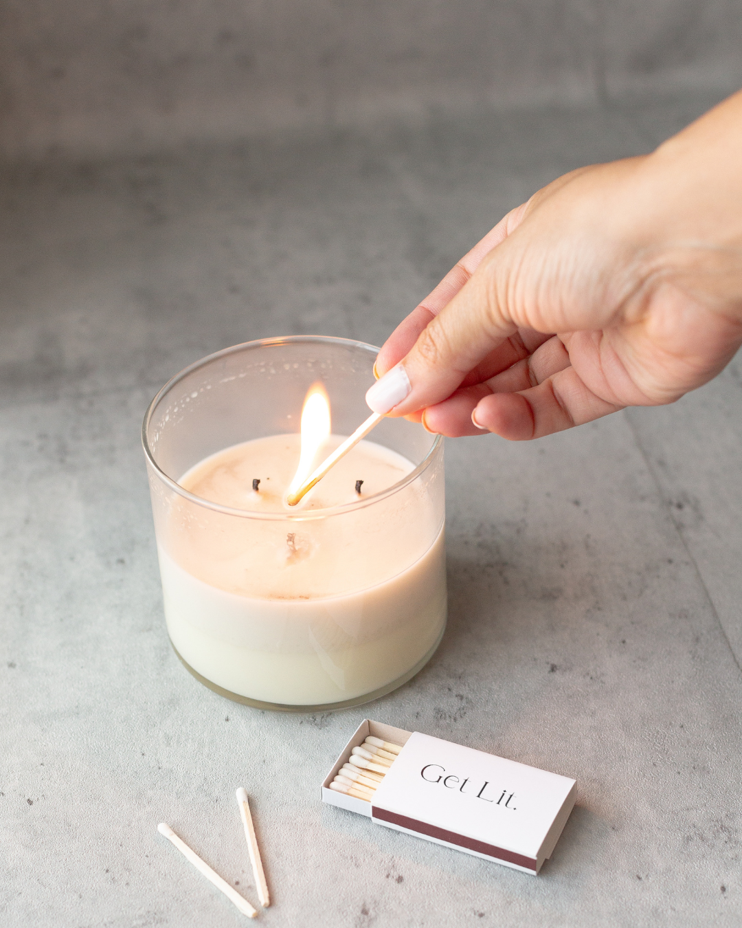 Hand lighting a candle with a match, with 'GOLDEN' matches visible on a gray surface.