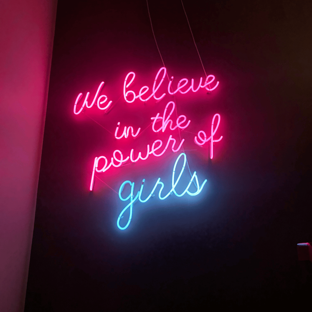 Neon sign with the text 'We believe in the power of girls' on a dark background