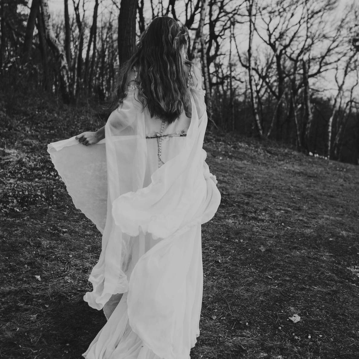 Woman in a flowing white gown walking through a dark forest, evoking a magical, otherworldly vibe perfect for fantasy books and fairytale-inspired stories.