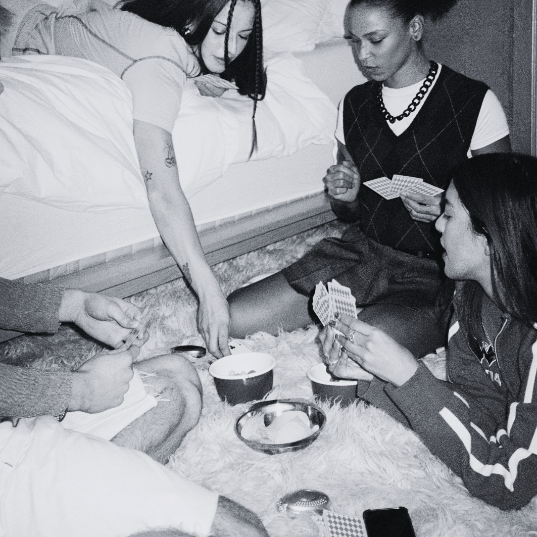 Group of teens sitting on the floor around a bed, playing cards and snacking, representing the fun, friendship, and drama found in young adult books.