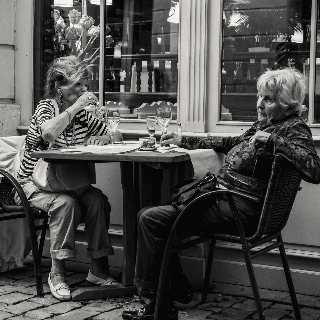 Two women sitting at a table outside a cafe, engaged in conversation.