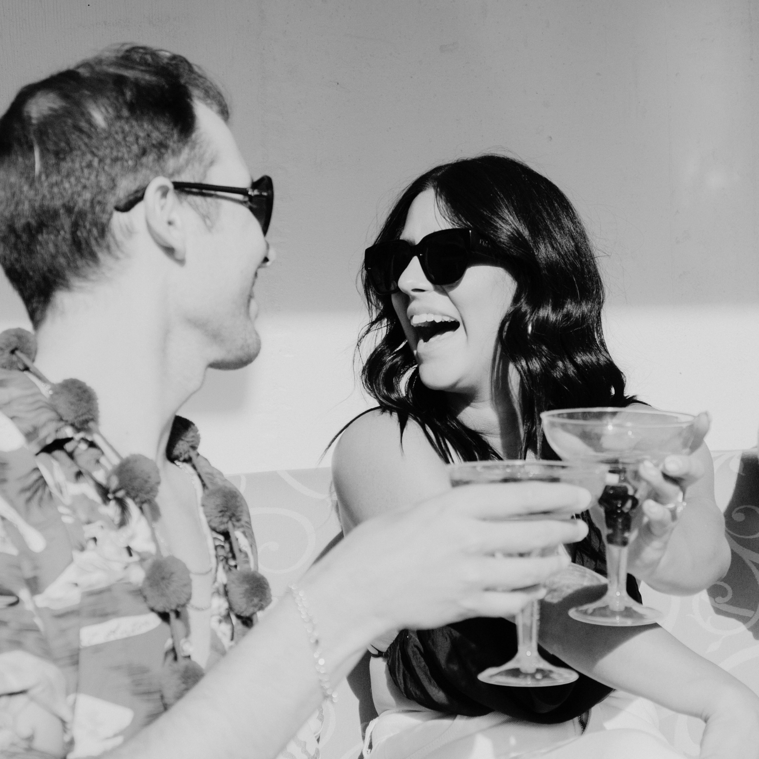 Two people sitting together, clinking cocktail glasses in a black and white photo.